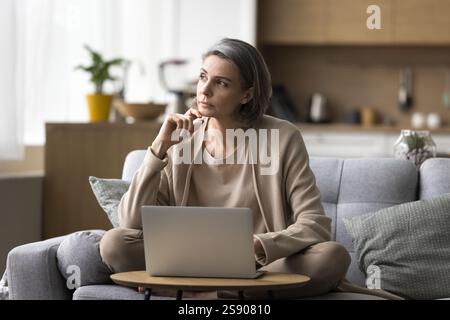 Femme mûre réfléchie travaillant à distance considérer distrait du carnet Banque D'Images