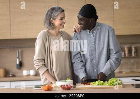Heureux couple multiethnique d'âge moyen préparer la salade à la cuisine à la maison Banque D'Images