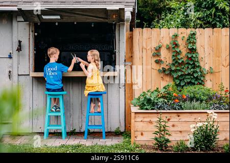 Deux enfants à un comptoir extérieur rustique, profitant d'une journée d'été. Banque D'Images
