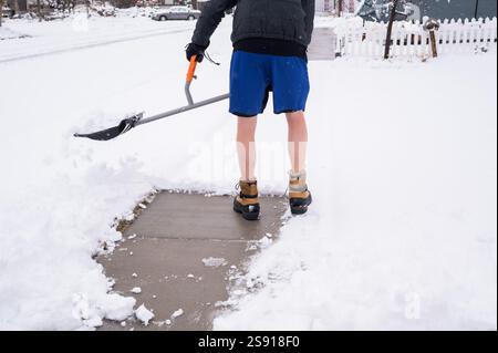 Homme pelletant la neige du trottoir dans un short de gym Banque D'Images