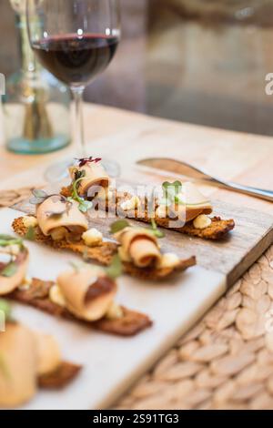 Hors-d'œuvre gastronomique sur une planche de bois rustique, élégamment plaqué avec pâté, fromage, microgreens et pain grillé croustillant, accompagné d'un verre de vin rouge Banque D'Images