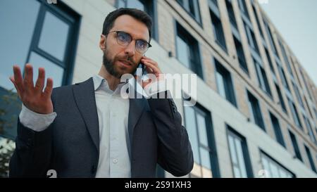 Insatisfait émotif homme d'affaires masculin homme d'affaires caucasien adulte homme d'affaires a choqué l'employé de bureau d'entrepreneur d'employeur parlant téléphone mobile à l'extérieur incroyable Banque D'Images