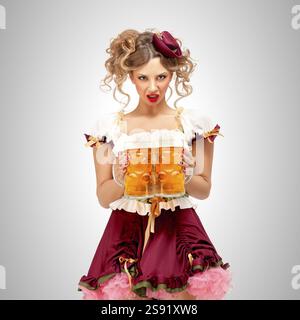 Belle serveuse Oktoberfest dans un dirndl bavarois traditionnel tenant des tasses à bière sur un fond gris Banque D'Images