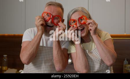 Drôle heureux grand-mère à la retraite grand-père caucasien vieille femme s'amusant ensemble faire des verres de paprika rouge poivrons cercles femme d'âge moyen mari vieux Banque D'Images