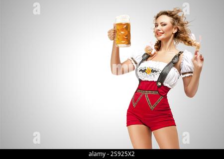 Belle femme en short pull-over rouge avec bretelles comme un dirndl traditionnel servant deux tasses à bière sur un fond gris Banque D'Images