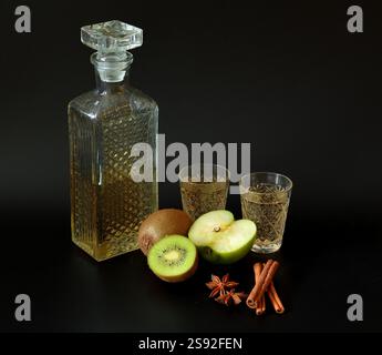 Kiwi et liqueur de pomme verte avec des épices en verre de cristal sur fond noir, morceaux de fruits mûrs, bâtonnets de cannelle et anis à proximité. Gros plan. Banque D'Images