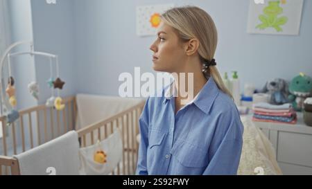 Femme assise dans une chambre à coucher à côté d'un berceau de bébé, avec une expression paisible, dans un cadre de maison confortable. Banque D'Images