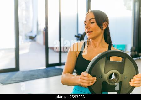 Une femme tient une plaque de musculation dans un gymnase. Elle est souriante et elle apprécie son entraînement Banque D'Images