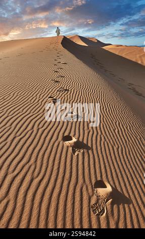 Homme marchant dans la belle Erg Chebbi Saharah Dunes de sable, Sahara, Maroc au lever du soleil paysage panoramique Banque D'Images