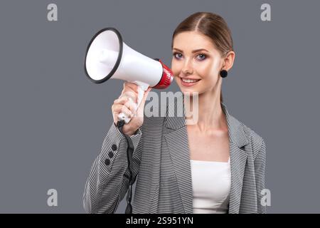 Une belle fille joyeuse crie dans le haut-parleur sur fond rose isolé. Banque D'Images