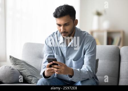 Jeune homme assis sur le canapé à l'aide du téléphone portable pour le travail en ligne Banque D'Images