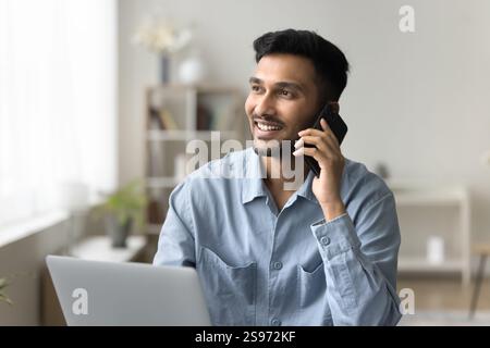 Homme souriant confiant répondre à un appel téléphonique assis à côté de l'ordinateur portable Banque D'Images