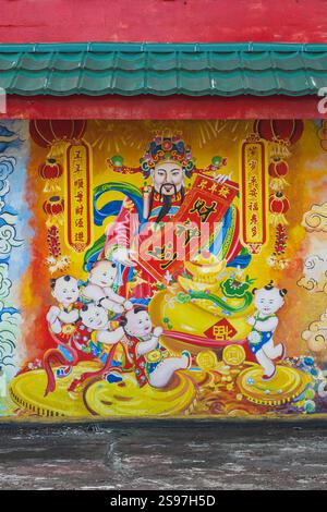 Balikpapan, Indonésie - 18 janvier 2025. La murale représente Caishen, le Dieu chinois de la richesse, tenant une bannière rouge au milieu d'une vague d'enfants an Banque D'Images
