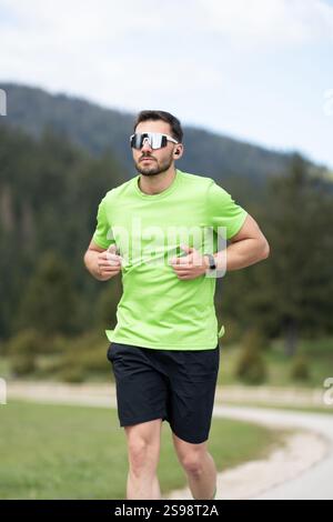 Runner in Green shirt et lunettes de soleil entraînement en plein air lors d'Une journée lumineuse avec la nature pittoresque qui l'entoure Banque D'Images