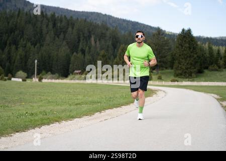 Runner in Green shirt et lunettes de soleil entraînement en plein air lors d'Une journée lumineuse avec la nature pittoresque qui l'entoure Banque D'Images