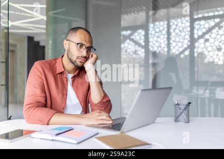 Fatigué homme ennuyé assis à l'ordinateur, employé de bureau à l'intérieur du bureau au lieu de travail. Surmené. Banque D'Images
