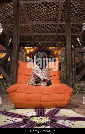 Gros plan de chien Labrador noir enveloppé dans une serviette assis dans une chaise orange luxueuse, fond d'effet de feu Banque D'Images