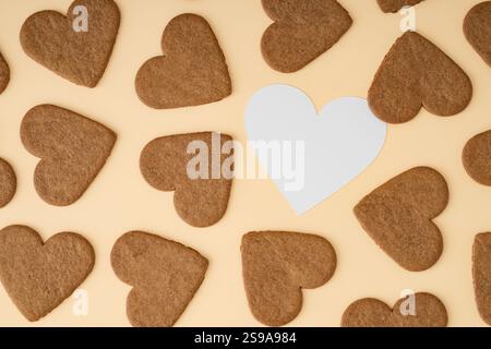 Modèle fait de biscuits en forme de coeur sur fond crème avec l'espace de copie de note de carte de papier. Disposition minimale de l'amour. Idée de biscuits créatifs. Banque D'Images