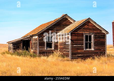 Une vieille maison en bois délabrée avec un toit incliné se dresse dans un champ d'herbe haute et sèche. La maison semble abandonnée et en mauvais état, avec pelage Banque D'Images