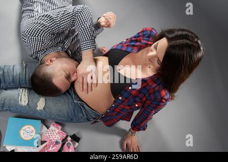 Mari aimant embrassant et touchant le ventre de sa femme enceinte alors qu'elle est assise à côté de lui, symbolisant l'anticipation et la connexion, isolé contre le gris b Banque D'Images