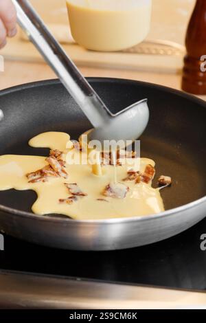 Garnir la pâte aux œufs et au bacon avec garnitures dans une poêle à frire pour la cuisson Banque D'Images