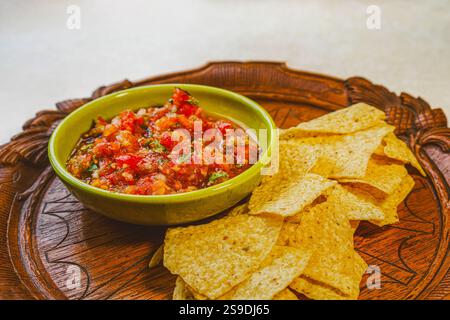 Salsa faite avec des tomates bio, de l'oignon et du basilic dans un bol vintage vert et servie avec des chips de maïs bio sur un plateau en bois antique. Banque D'Images