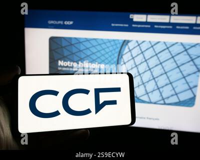 Dans cette illustration photo, une personne tient un téléphone portable avec le logo de la société crédit commercial de France (CCF) sur l'écran devant la page web de l'entreprise. Banque D'Images