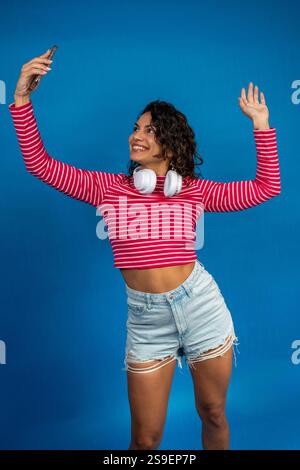 Influenceuse heureuse créant du contenu pour les médias sociaux, prenant un selfie et agitant ses followers Banque D'Images