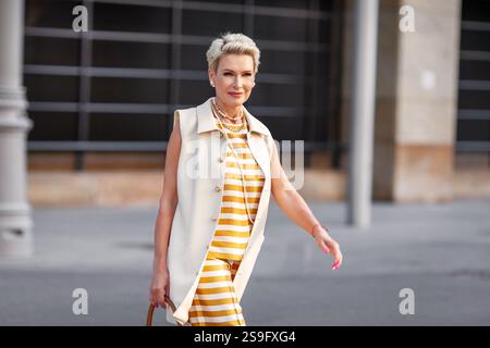 Femme d'affaires mature élégante avec les cheveux courts en gilet blanc élégant Workwear, pantalon rayé jaune et blanc et collier de perles marchant à l'extérieur dans CIT Banque D'Images