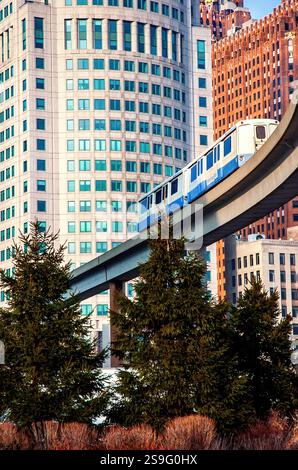 Le train de banlieue traverse un pont devant un grand bâtiment. Le train est bleu Banque D'Images