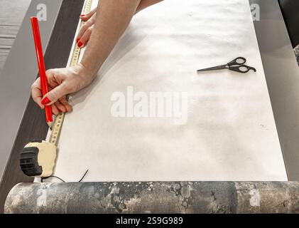 Couper le papier peint avant de le coller au mur, ciseaux, ruban à mesurer et crayon sur la table, couper le papier peint à la taille Banque D'Images