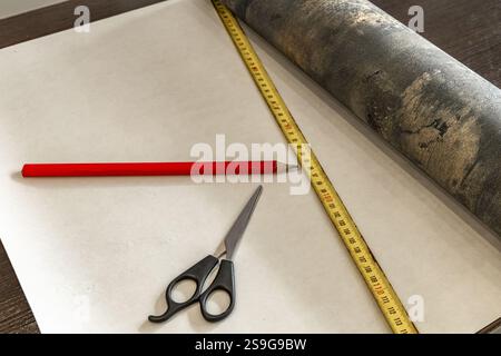 Couper le papier peint avant de le coller au mur, ciseaux, ruban à mesurer et crayon sur la table, couper le papier peint à la taille Banque D'Images