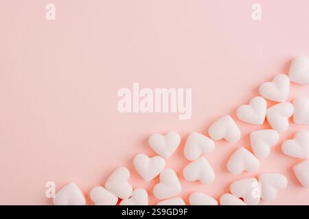 Bonbons blancs en forme de coeur dispersés sur un fond rose pastel, symbolisant la douceur et l'amour. Concept de la Saint-Valentin. Vue de dessus, plat, spa de copie Banque D'Images