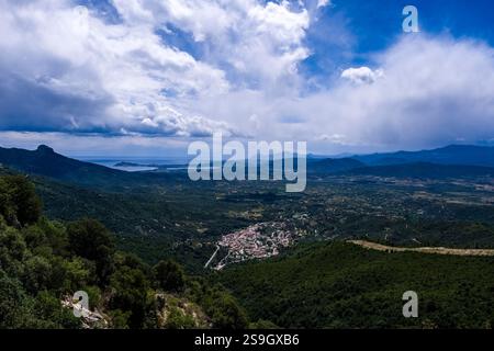Vue aérienne de la petite ville de Talana, située sur une colline boisée, avec la mer Méditerranée et les chaînes de montagnes au loin. Banque D'Images