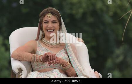 belle mariée caucasienne joyeuse en tenue de mariée indienne riant comme sa chaise est soulevée dans la tradition hindoue de cérémonie de mariage Banque D'Images