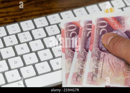 Main tenant des livres sterling au-dessus d'un clavier d'ordinateur blanc. Concept financier. Achats en ligne. Monnaie britannique, trading de devises GBP Banque D'Images