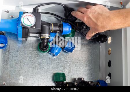 Un homme installe un système d'irrigation goutte à goutte en plaçant des composants automatiques dans une boîte métallique. Banque D'Images