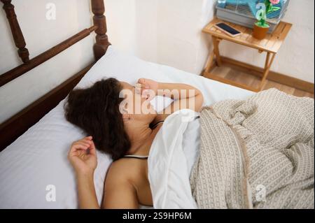 Un moment paisible montrant une femme endormie dans un lit confortable avec de la lumière naturelle. Le cadre représente la sérénité et la détente, mettant l'accent sur un sommeil réparateur et Banque D'Images