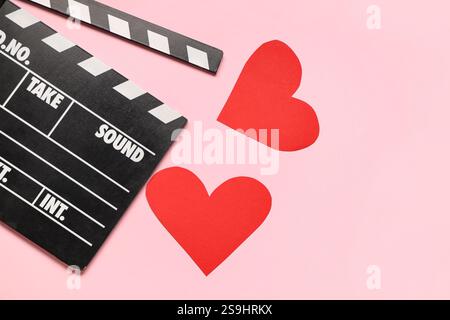 Film clapper et coeurs de papier sur fond rose. Fête de la Saint-Valentin Banque D'Images