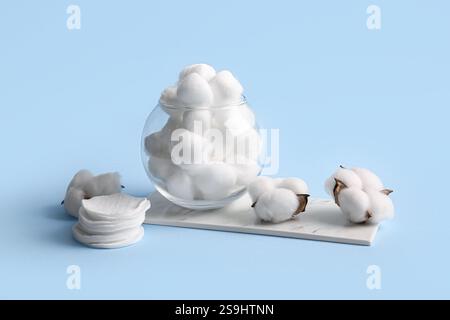 Verre avec des boules de coton, des tampons et des fleurs sur fond bleu Banque D'Images