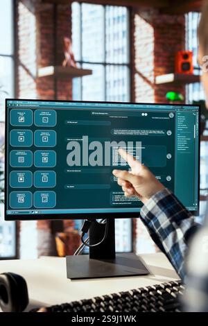 Employé distant assis au bureau obtenant de l'aide du logiciel chatbot ai LLM dans le bureau à domicile. Homme pointant vers l'écran, travaillant avec un grand programme de modèle de langage sur le moniteur d'ordinateur Banque D'Images