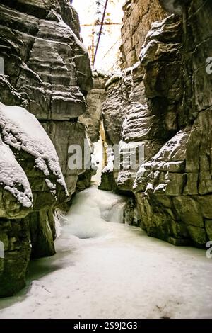 Un étroit canyon enneigé avec un petit ruisseau qui le traverse. La neige s’accumule sur les rochers, créant une sensation de profondeur et d’isolement. Le Banque D'Images