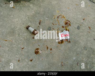 Fermer vue de dessus d'une bouteille de bière Coors Light en verre brun brisé sur un trottoir en béton. Étiquette de goulot et de goulot de bouteille avec morceaux. Utilisation éditoriale sur Banque D'Images