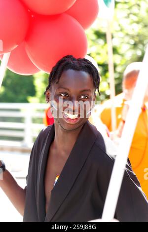Jeune homme noir souriant tenant des ballons rouges à Birmingham gay Pride célébrant la diversité et l'égalité LGBT+ Banque D'Images
