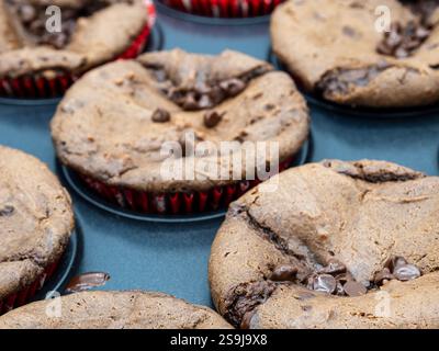 Une vue rapprochée de brownies au chocolat riches et fugaces nichés dans des formes de papier rouge vif, reposant sur une plaque de cuisson, mettant en valeur leur texture irrésistible Banque D'Images