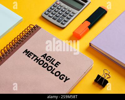 Cahier avec méthodologie agile écrit sur la couverture, accompagné d'une calculatrice, surligneur, clip de reliure et notes adhésives, incarnant la gestion de projet c Banque D'Images