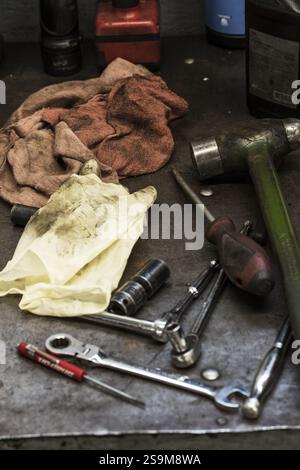 boîte à outils de mécanicien graisseux comprenant des chiffons, des clés, un marteau, un jeu de douilles et des tournevis sur le sol d'un garage en service Banque D'Images