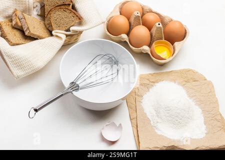 Fouetter dans le bol. Farine sur papier. Oeufs dans un récipient en carton. Toast sur serviette blanche. Fond blanc. Vue de dessus Banque D'Images