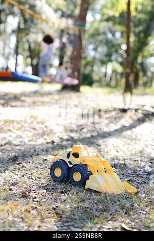 Bulldozer jouet jaune sur un sol herbeux avec des enfants jouant en t Banque D'Images