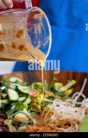 Garçon versant la vinaigrette aux cacahuètes sur la salade de nouilles et de légumes Banque D'Images